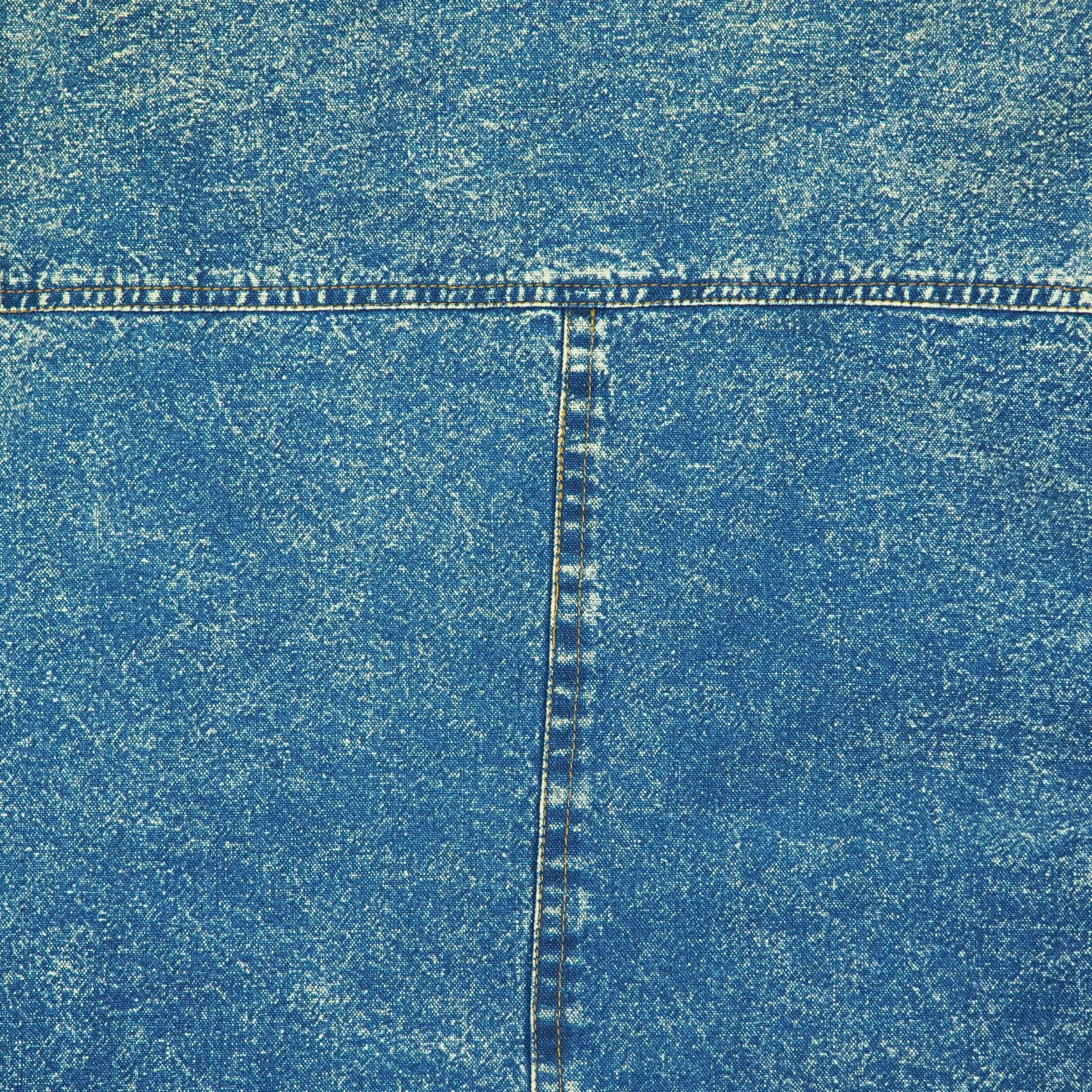 Close-up of back of an acid wash blue denim shirt with a visible T seam with orange stitching.