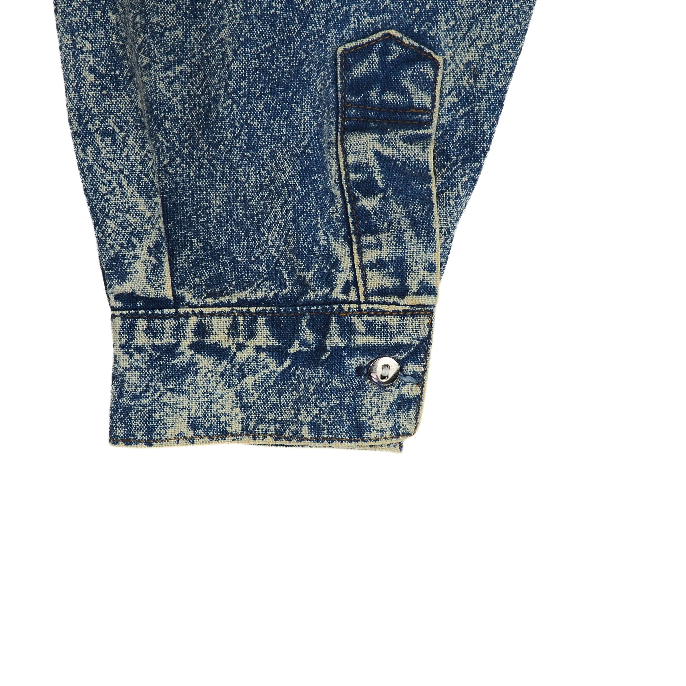 Close-up of a acid wash blue denim shirt sleeve cuff with a metallic silver button on a white background