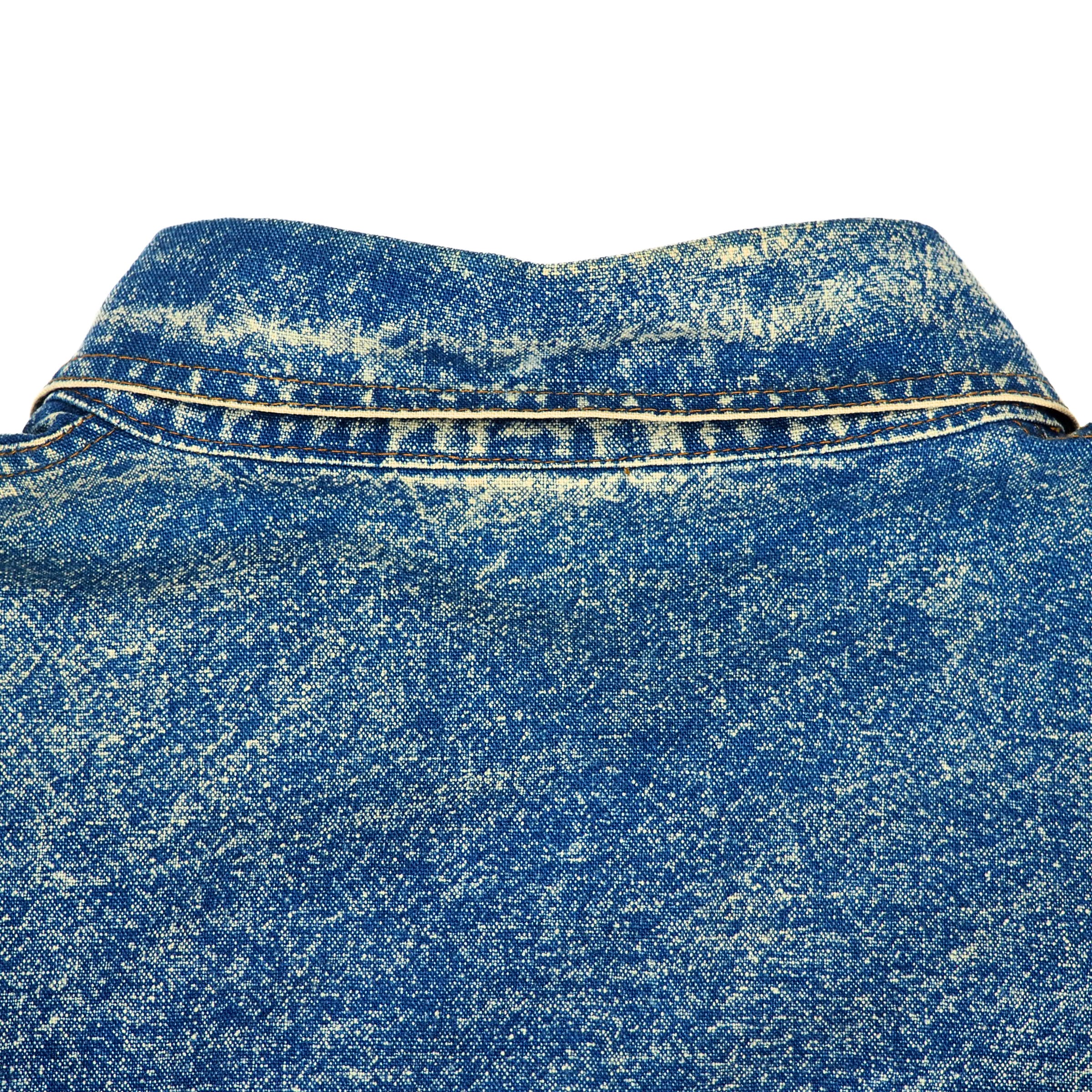 Close-up focusing on patina and texture of a vintage blue acid wash denim shirt collar with orange stitching on a white background.