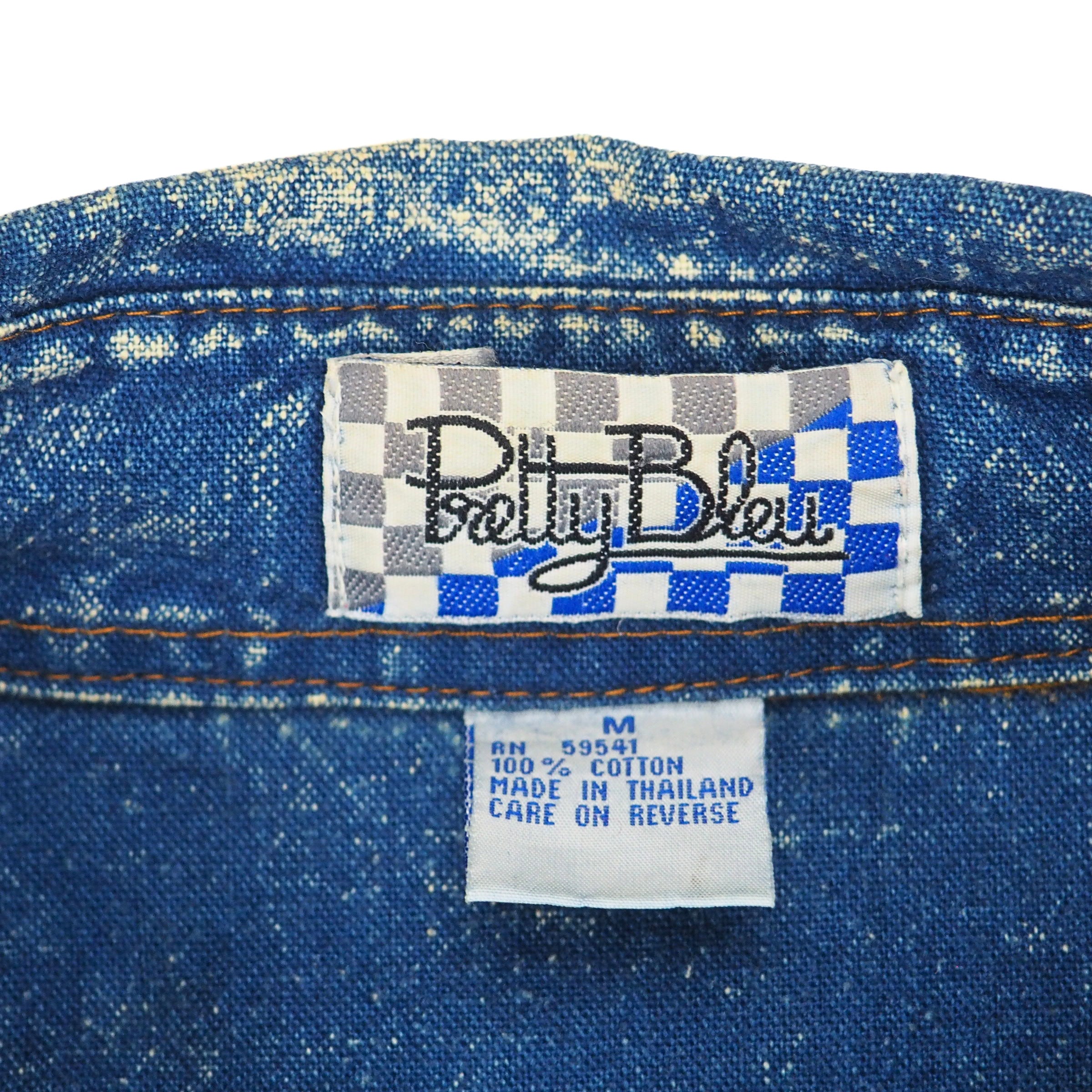 Close-up of a blue denim shirt with 'Pretty Blue' label branding on a white background.