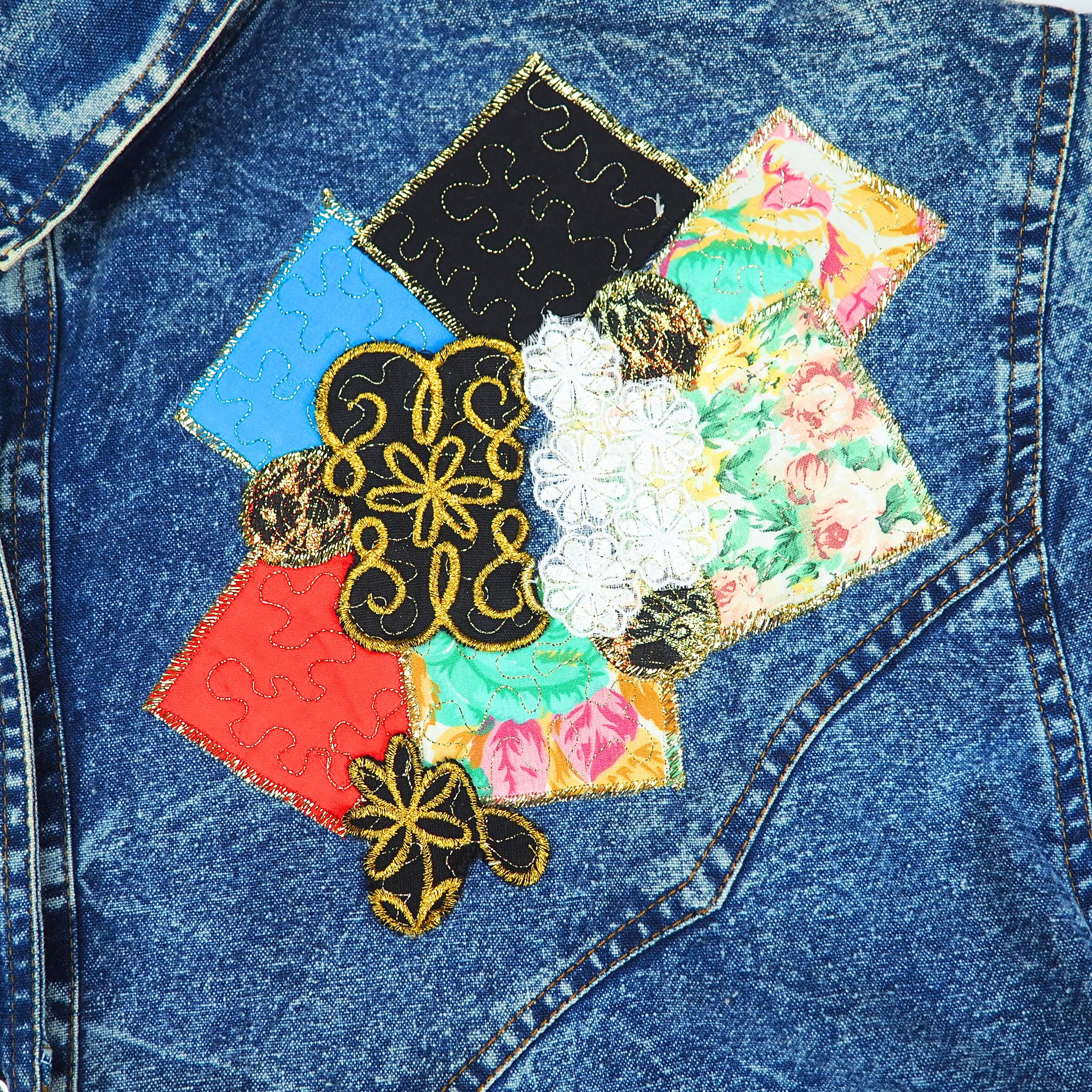 Close-up detail of a vintage denim shirt with colorful patchwork design and embroidery.