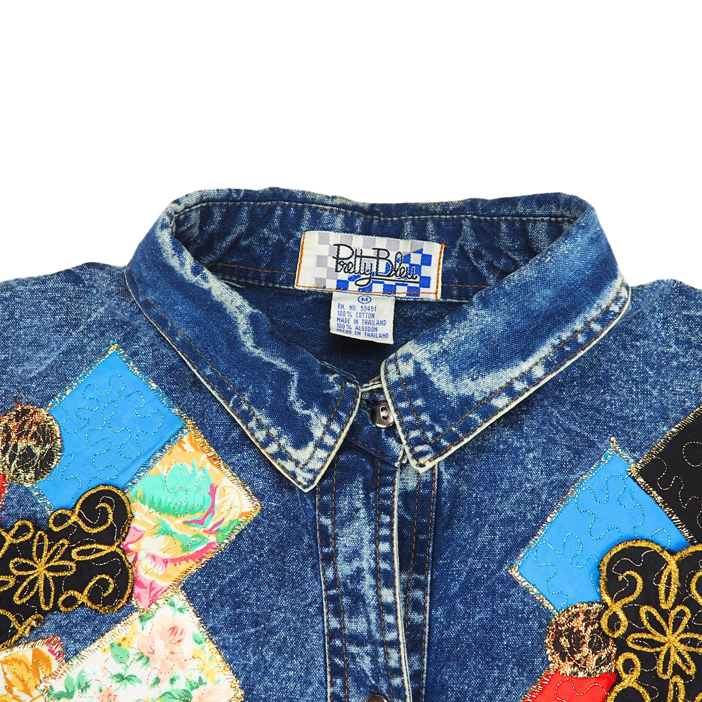 Collar detail of a vintage denim shirt with colorful patchwork design on a white background
