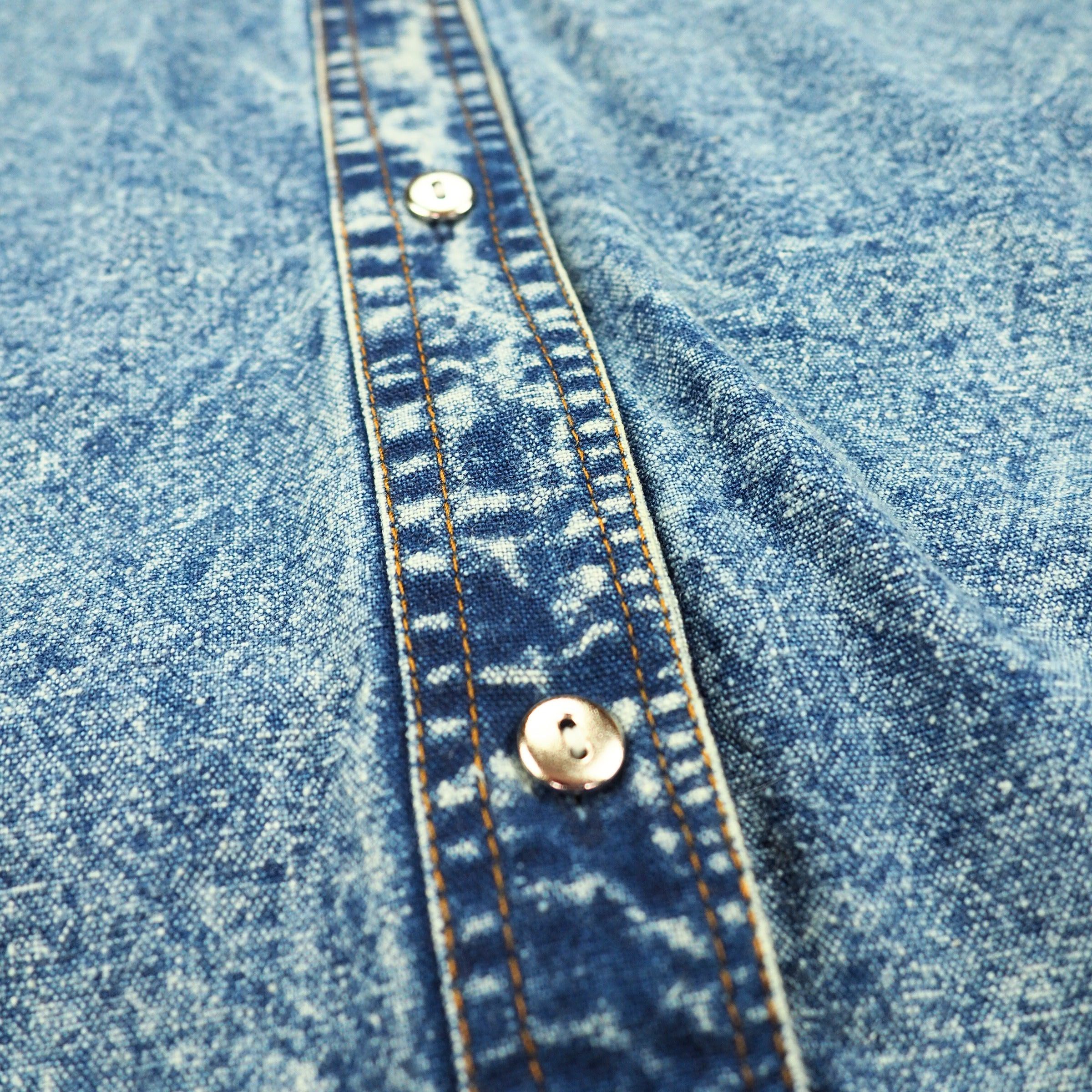 Close-up of blue acid wash denim fabric with orange stitching and silver buttons