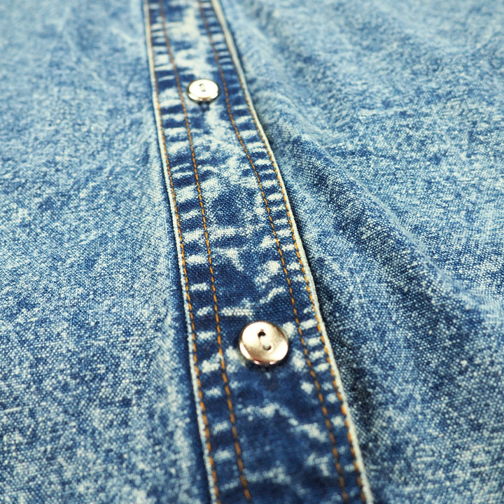Close-up of blue acid wash denim fabric with orange stitching and silver buttons