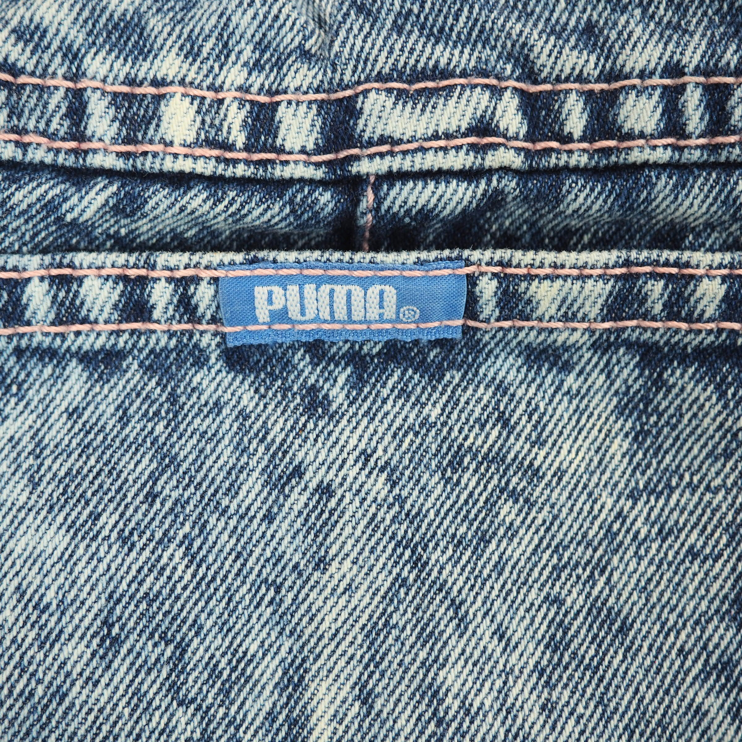 Close-up of a Puma label on blue denim fabric with pink stitching.