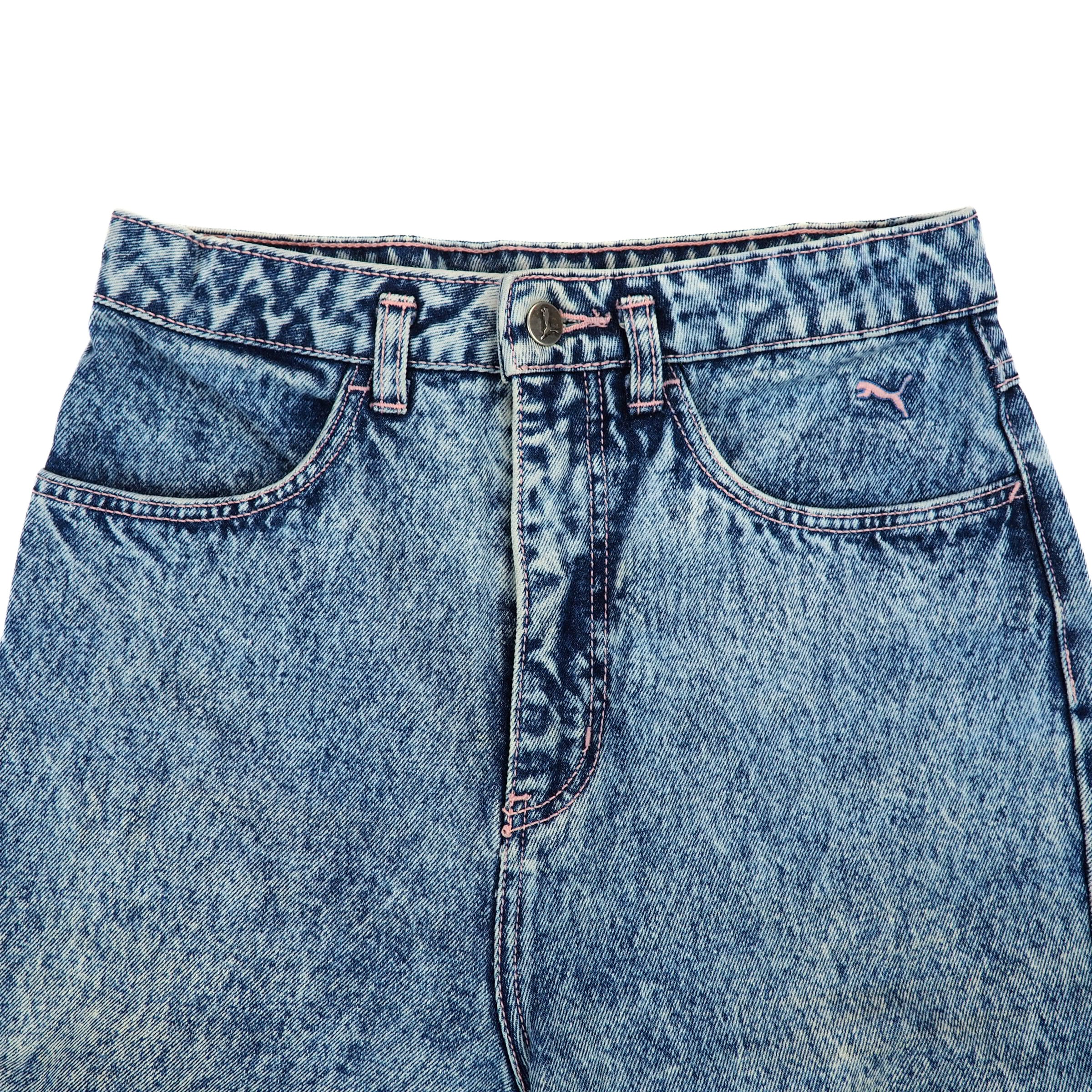 Close up of the front waist area of a pair of blue denim jeans with a Puma brand logo on a white background