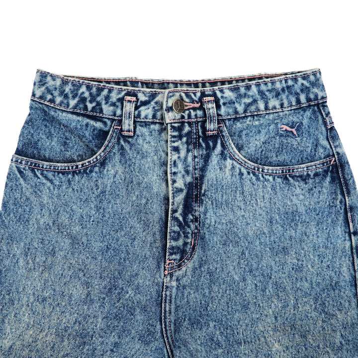 Close up of the front waist area of a pair of blue denim jeans with a Puma brand logo on a white background