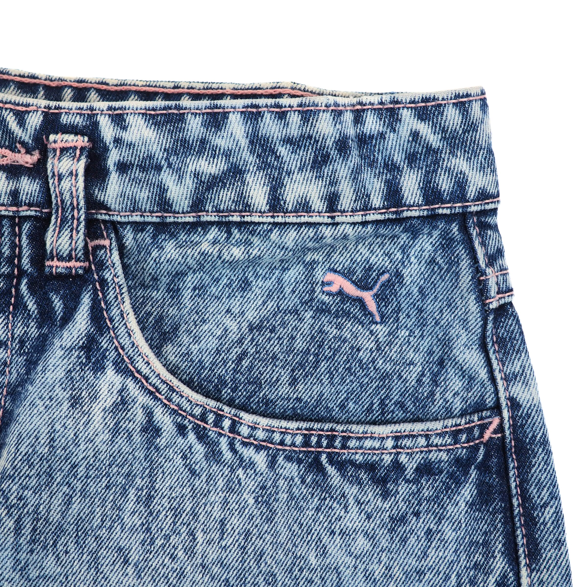 Close-up of blue denim jeans waist and pocket with a Puma brand logo and pink stitching on a white background.