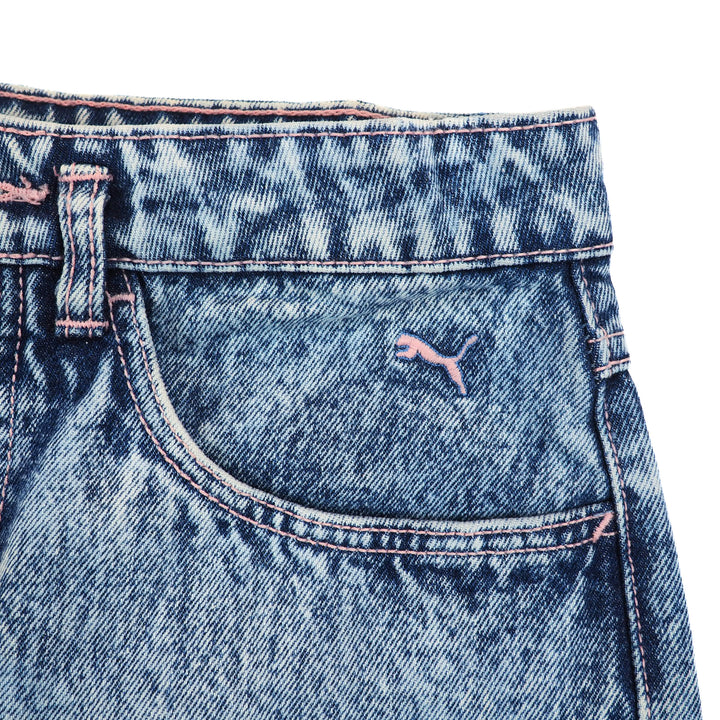 Close-up of blue denim jeans waist and pocket with a Puma brand logo and pink stitching on a white background.