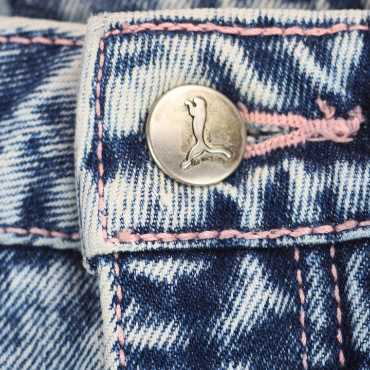 Close-up of a silver button and pink stitching on a pair of denim jeans.