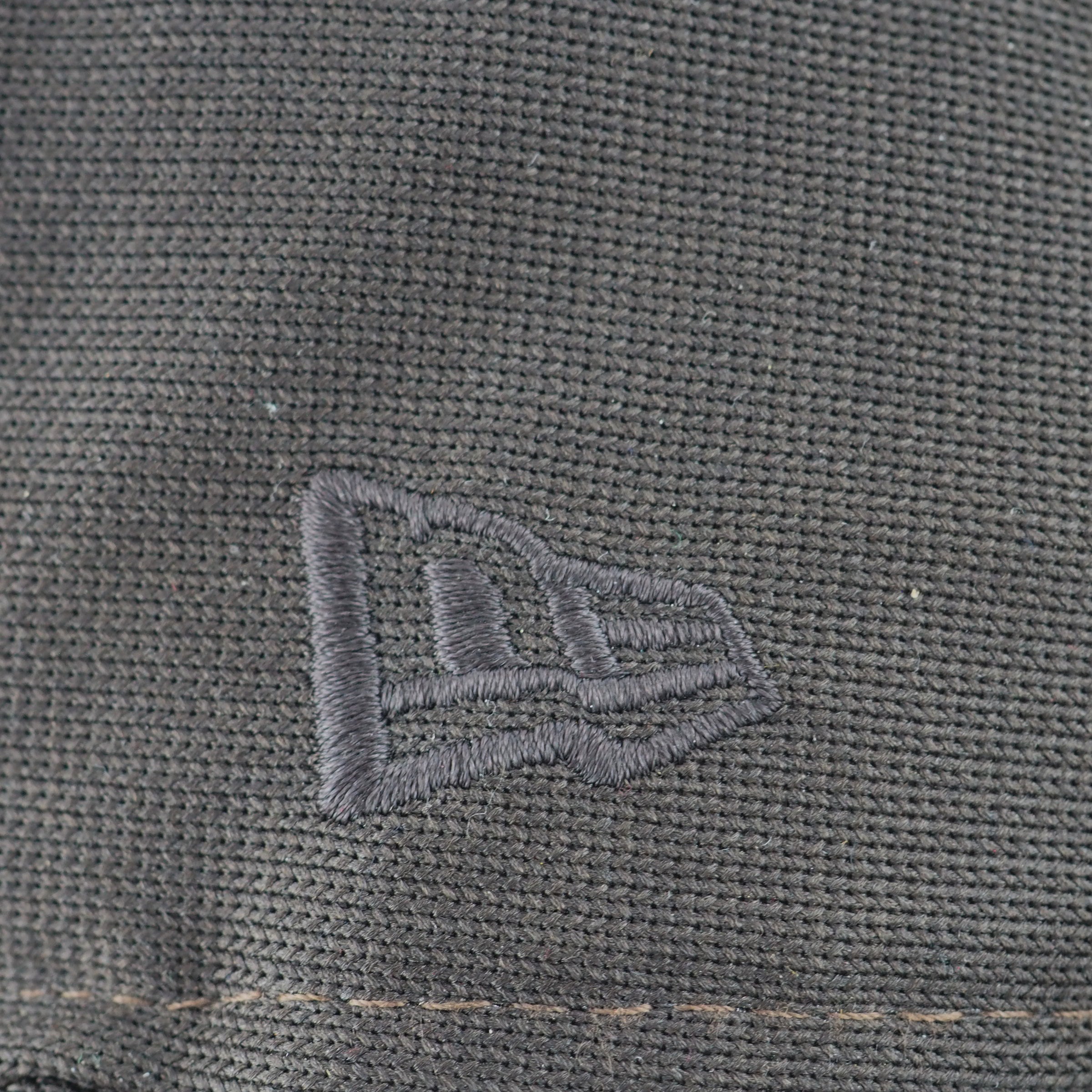 Close-up of a textured gray fabric with a New Era brand logo embroidered on it.