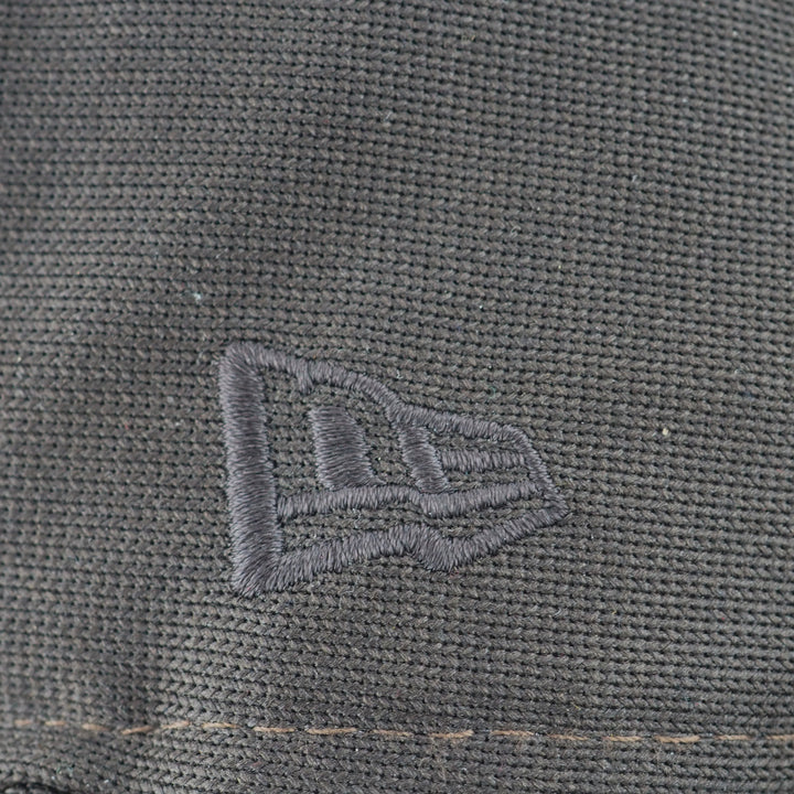 Close-up of a textured gray fabric with a New Era brand logo embroidered on it.