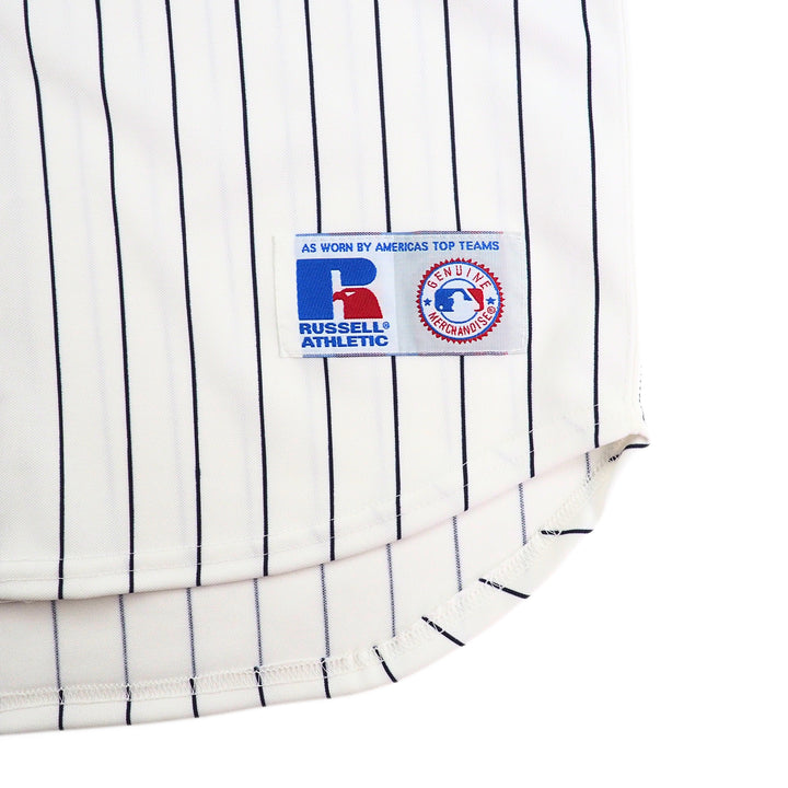 Close-up of a white Yankees baseball jersey with navy pinstripes and Russell Athletic logo.