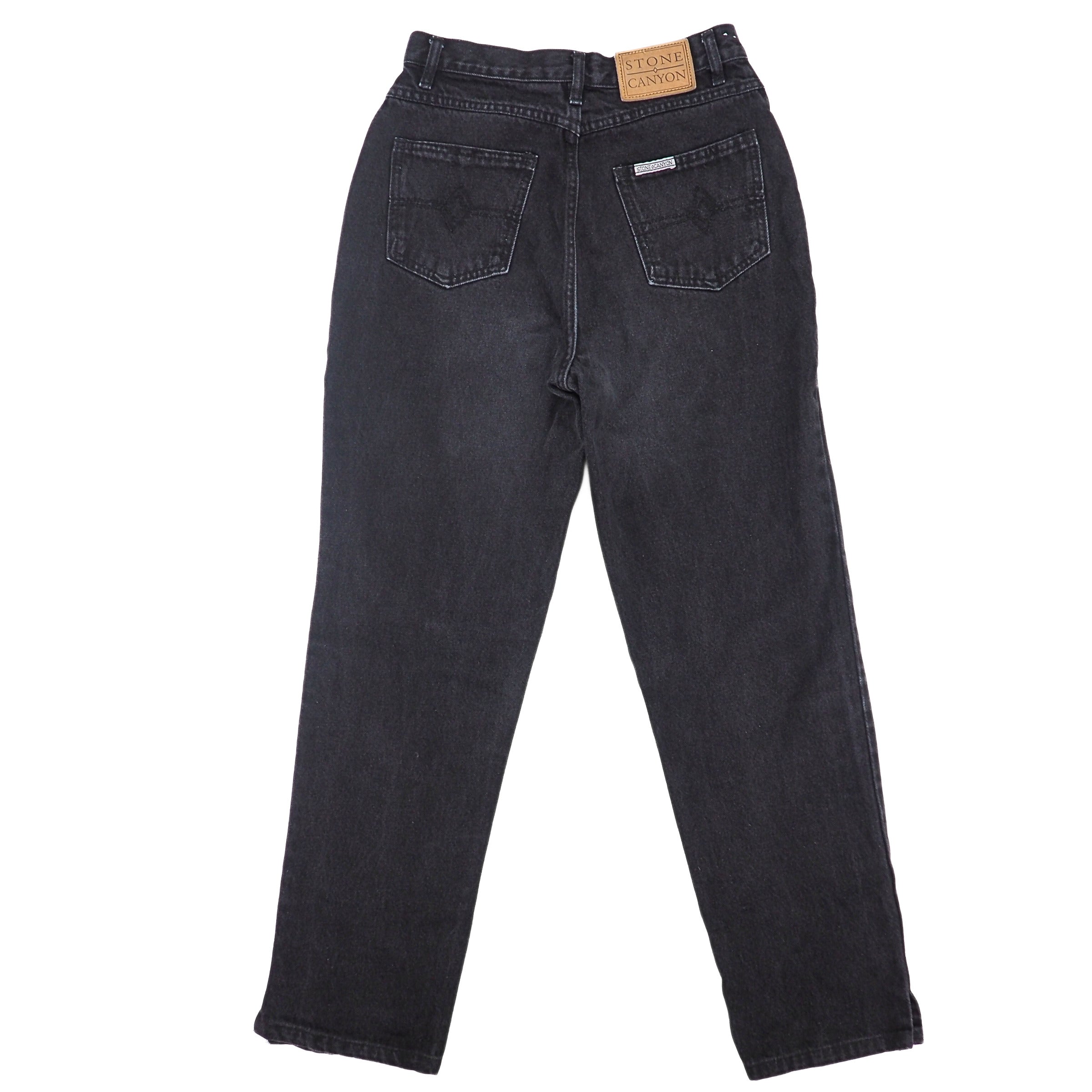 Back view of a pair of black denim jeans on a white background