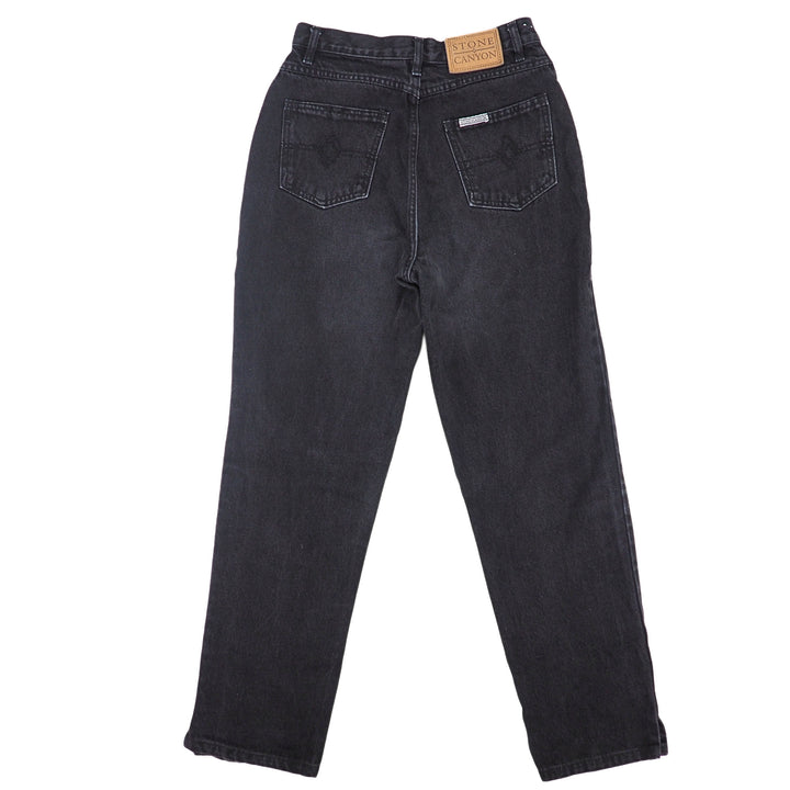 Back view of a pair of black denim jeans on a white background
