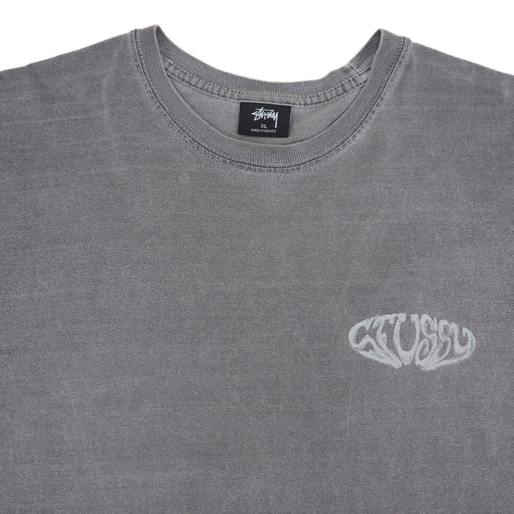 A close-up of a gray Stüssy crewneck t-shirt featuring a white Stüssy logo on the left chest, with the brand's black neck label visible inside the collar.