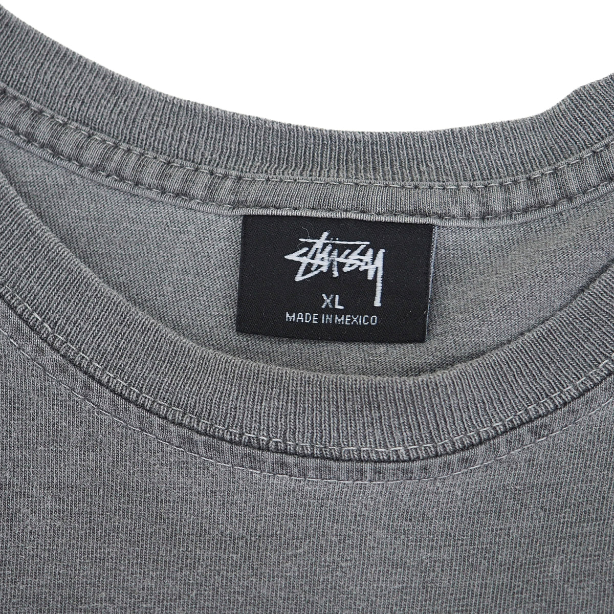 Close-up of a gray ribbed crewneck t-shirt showing the black Stussy brand label inside the collar.