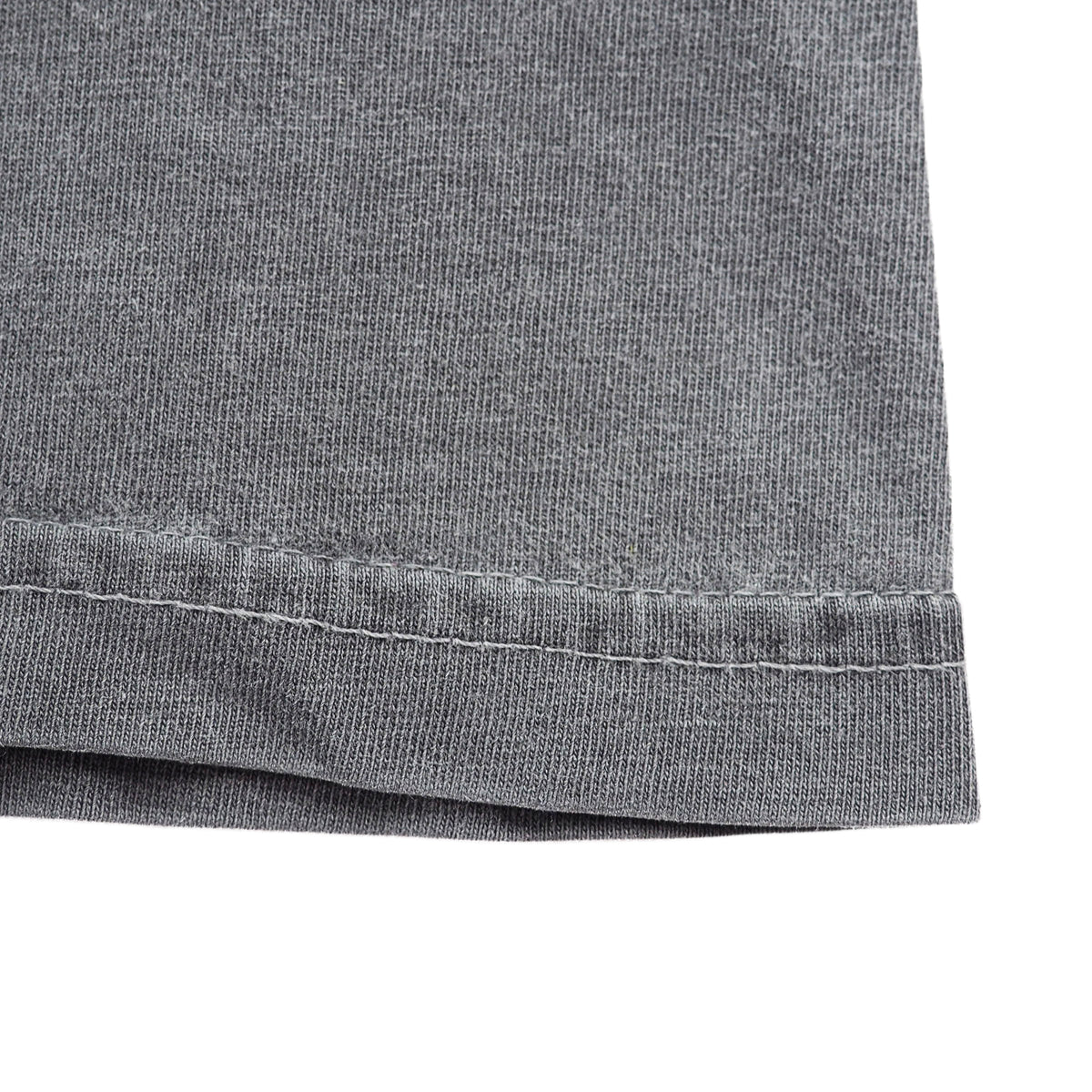 Close-up detail of the hem of a washed grey t-shirt, showing the hem and stitching against a white background.
