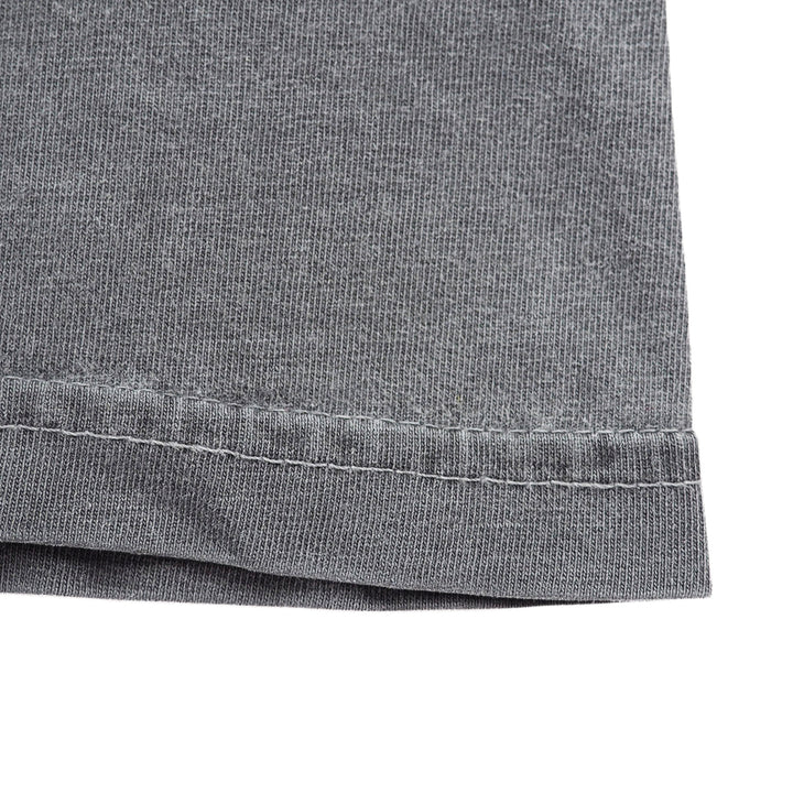 Close-up detail of the hem of a washed grey t-shirt, showing the hem and stitching against a white background.