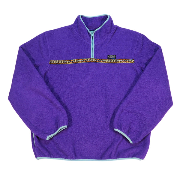 A purple fleece quarter-zip pullover jacket with a light blue zipper, light blue trim, and a decorative horizontal patterned stripe across the chest. A small black Stussy logo is visible on the chest.