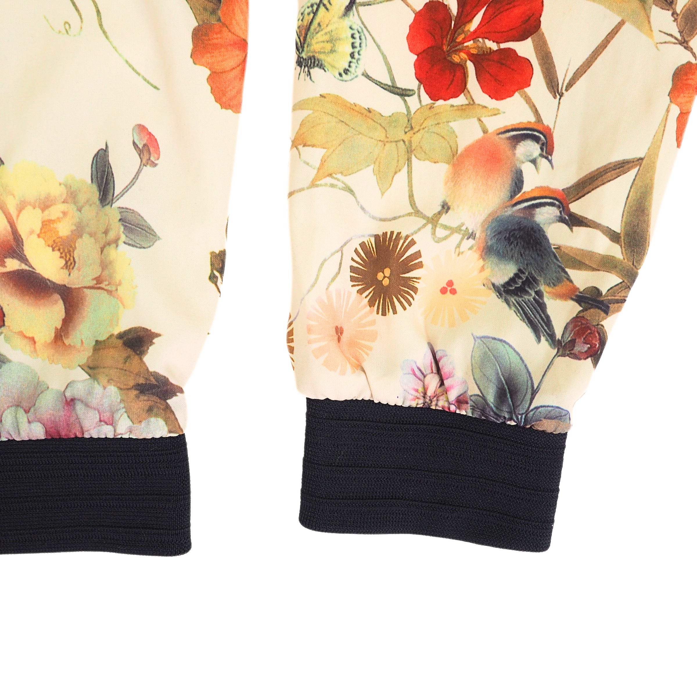 Sleeve and body detail of a jacket with floral and bird patterns and black cuffs on a white background