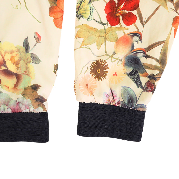 Sleeve and body detail of a jacket with floral and bird patterns and black cuffs on a white background