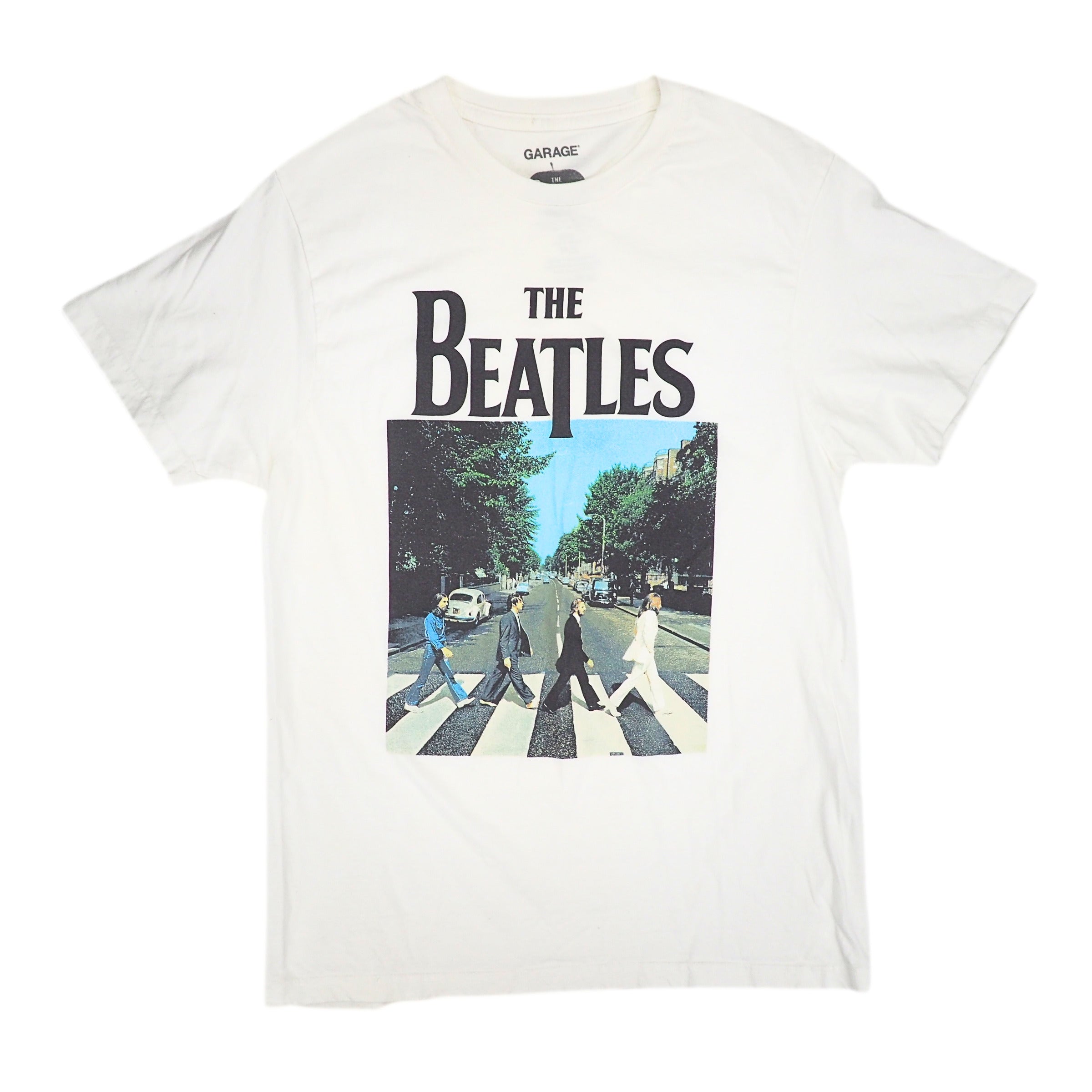 An off-white short-sleeve t-shirt featuring a large graphic print of The Beatles' 'Abbey Road' album cover on the front, with 'THE BEATLES' text above the square album artwork. The inner neck label reads 'GARAGE'.