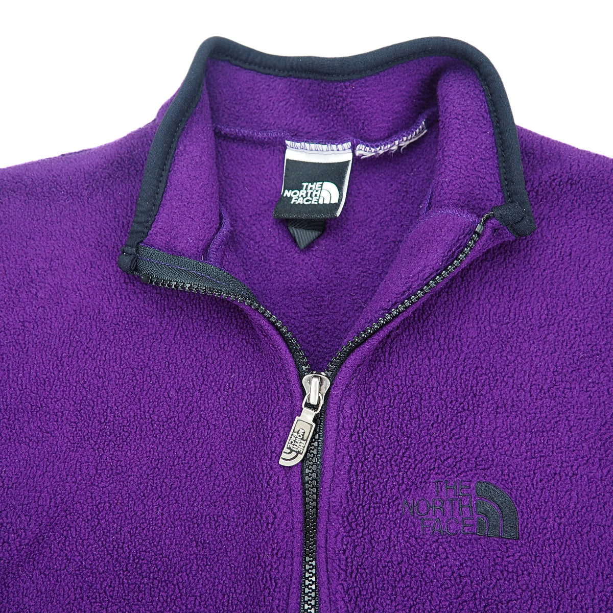 Close up of the open neck and front zipper of a vintage The North Face fleece vest in purple with black trim on a white background.