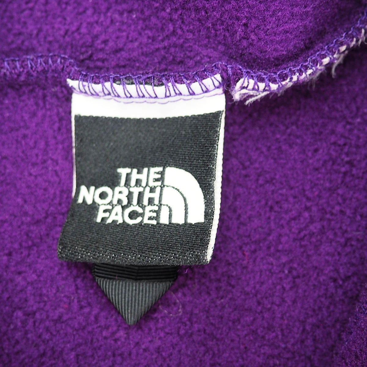 Close up of a black and white The North Face brand label on the inside of a purple fleece garment.