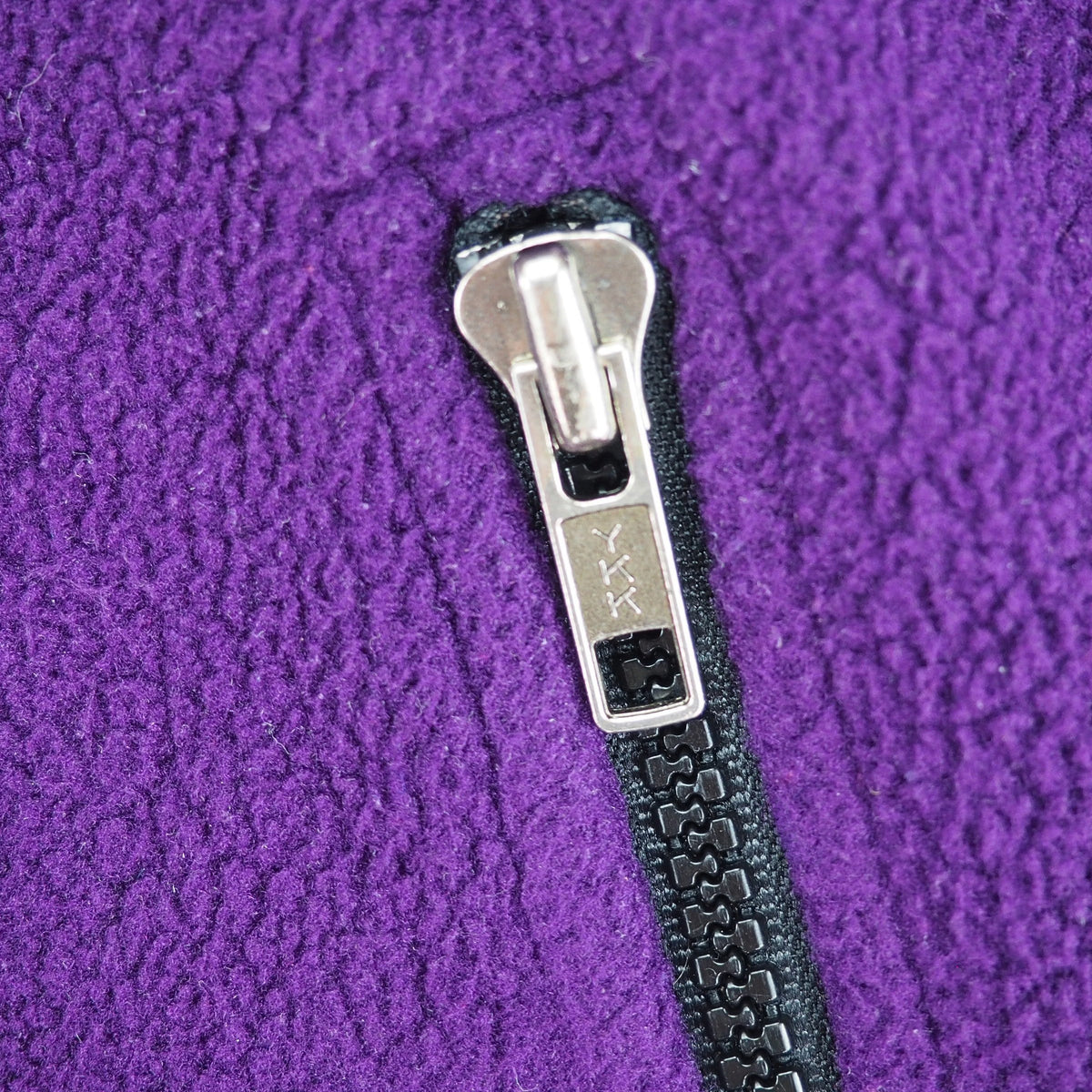 Close up of a silver and black ykk zipper pocket on a purple fleece vest.