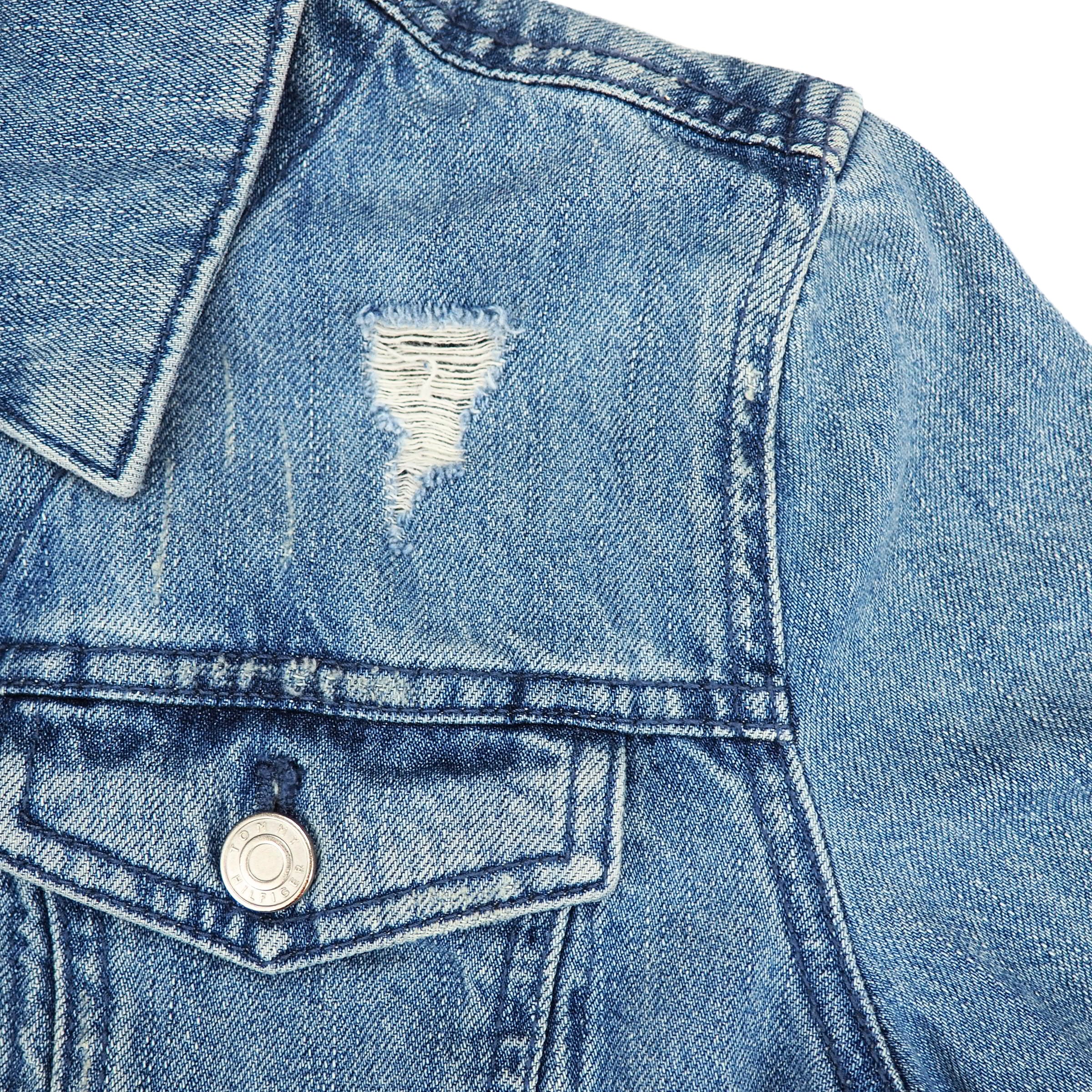 Close-up of a blue denim jacket shoulder and pocket with a button and distressed area.