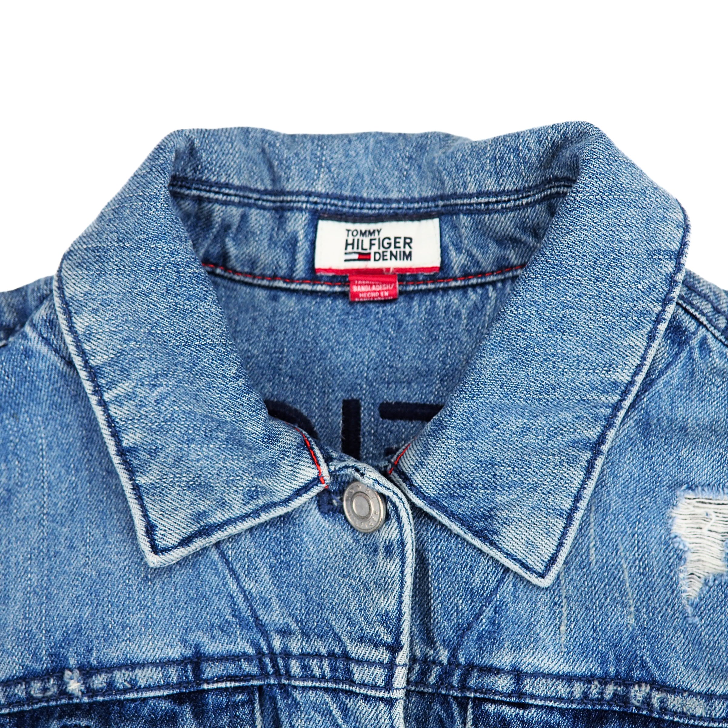 Close-up of a blue denim jacket collar with a Tommy Hilfiger label on a white background
