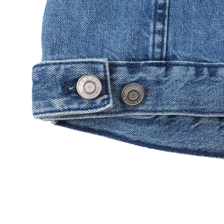Close-up of a blue denim jacket hem with stamped 'Tommy Hilfiger' button details on a white background