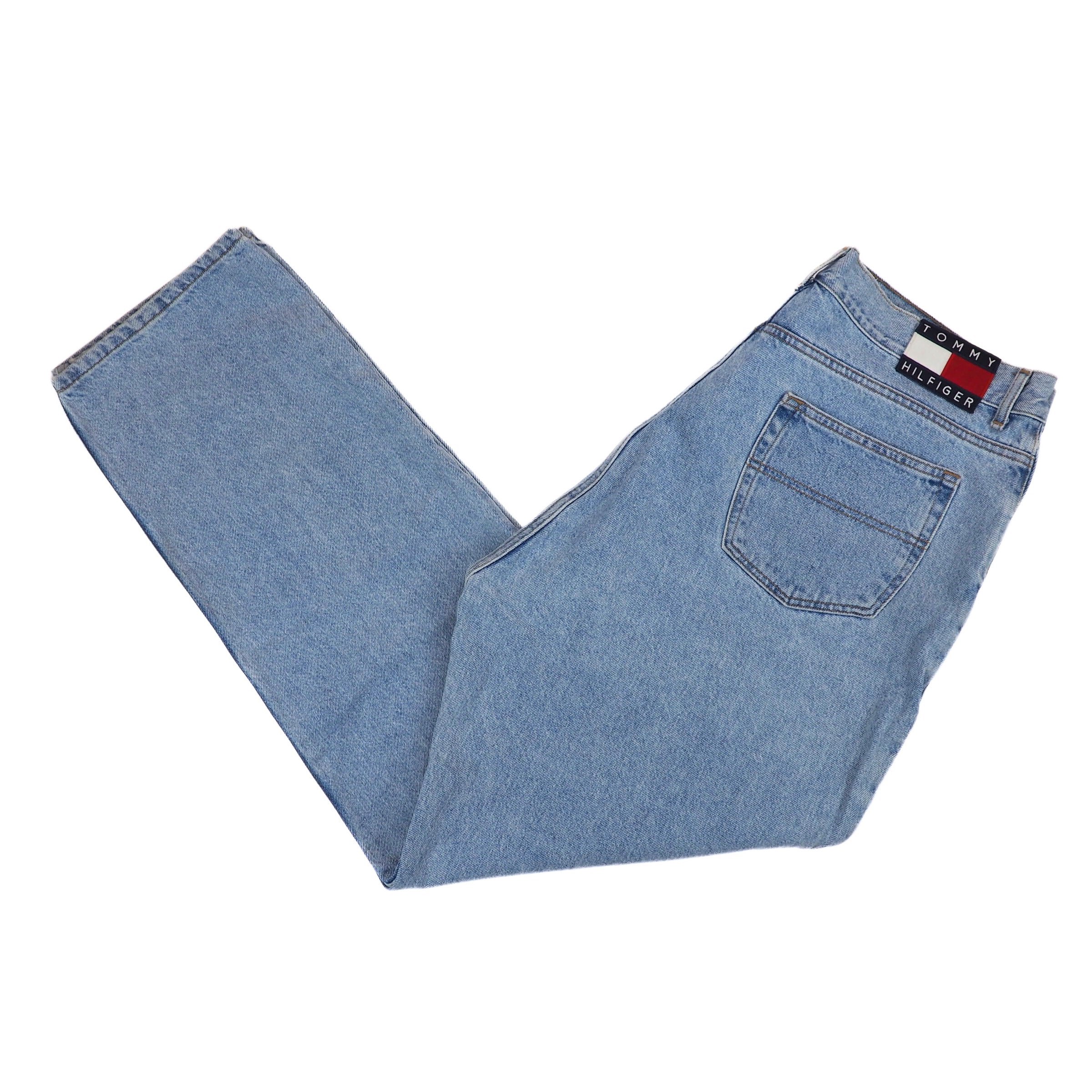 Folded light blue jeans with a Tommy Hilfiger flag brand label on a white background