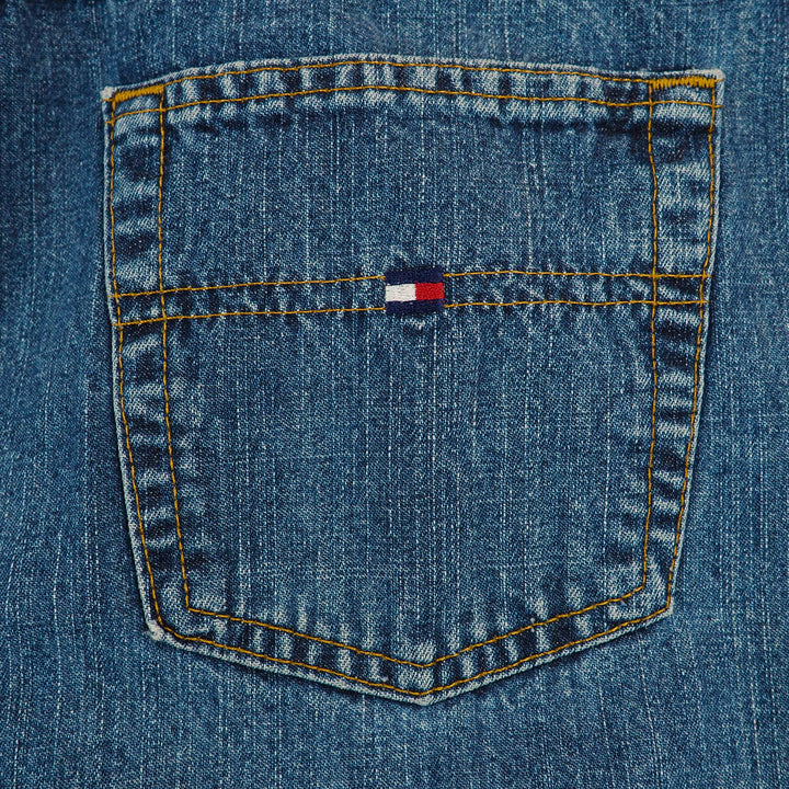 Close-up of a blue denim jean pocket with a Tommy Hilfiger flag logo and orange stitching.