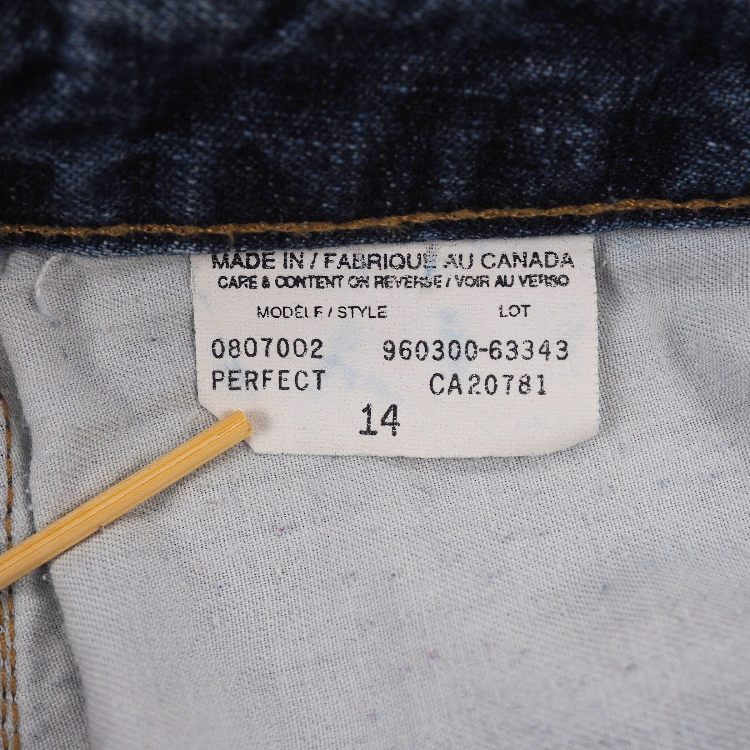 Close-up of a white clothing care label on fabric with black text and numbers.