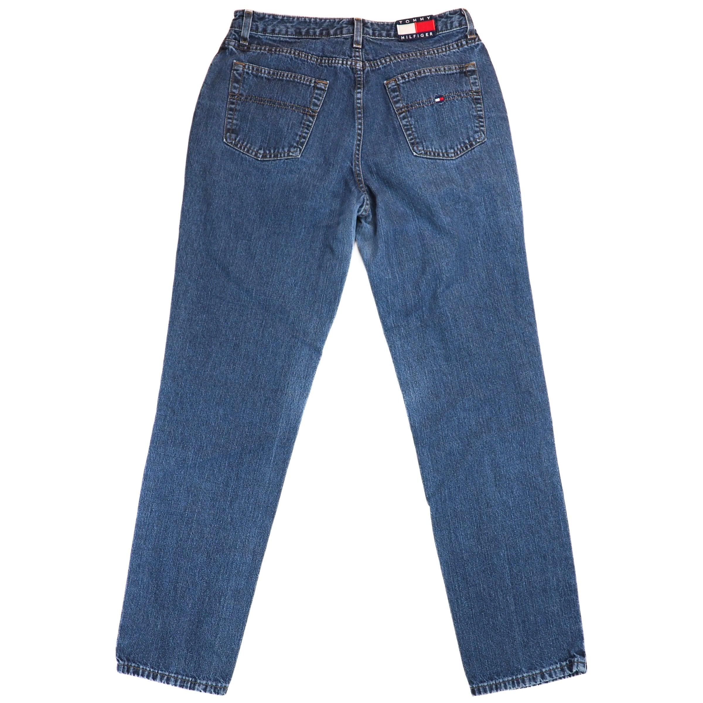 Back view of a pair of blue jeans with a Tommy Hilfiger brand logo on a white background