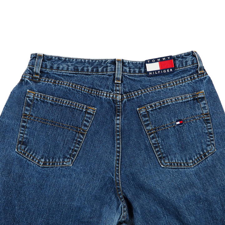 Back view close up of the pockets and waist of a pair of blue jeans with Tommy Hilfiger logo on a white background.