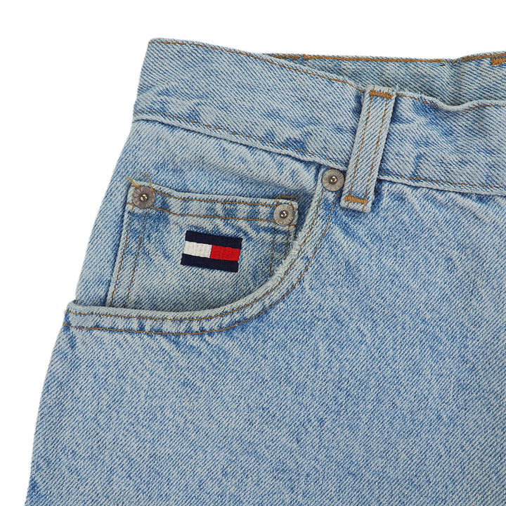 Close-up of a blue denim jean coin pocket with a Tommy Hilfiger flag logo on a white background