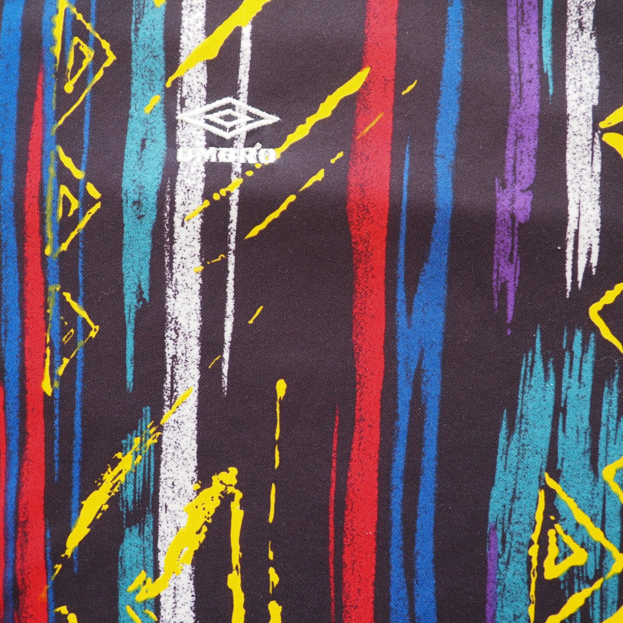 Colorful abstract pattern with vertical lines and geometric shapes and an embroidered 'Umbro' logo on a black background