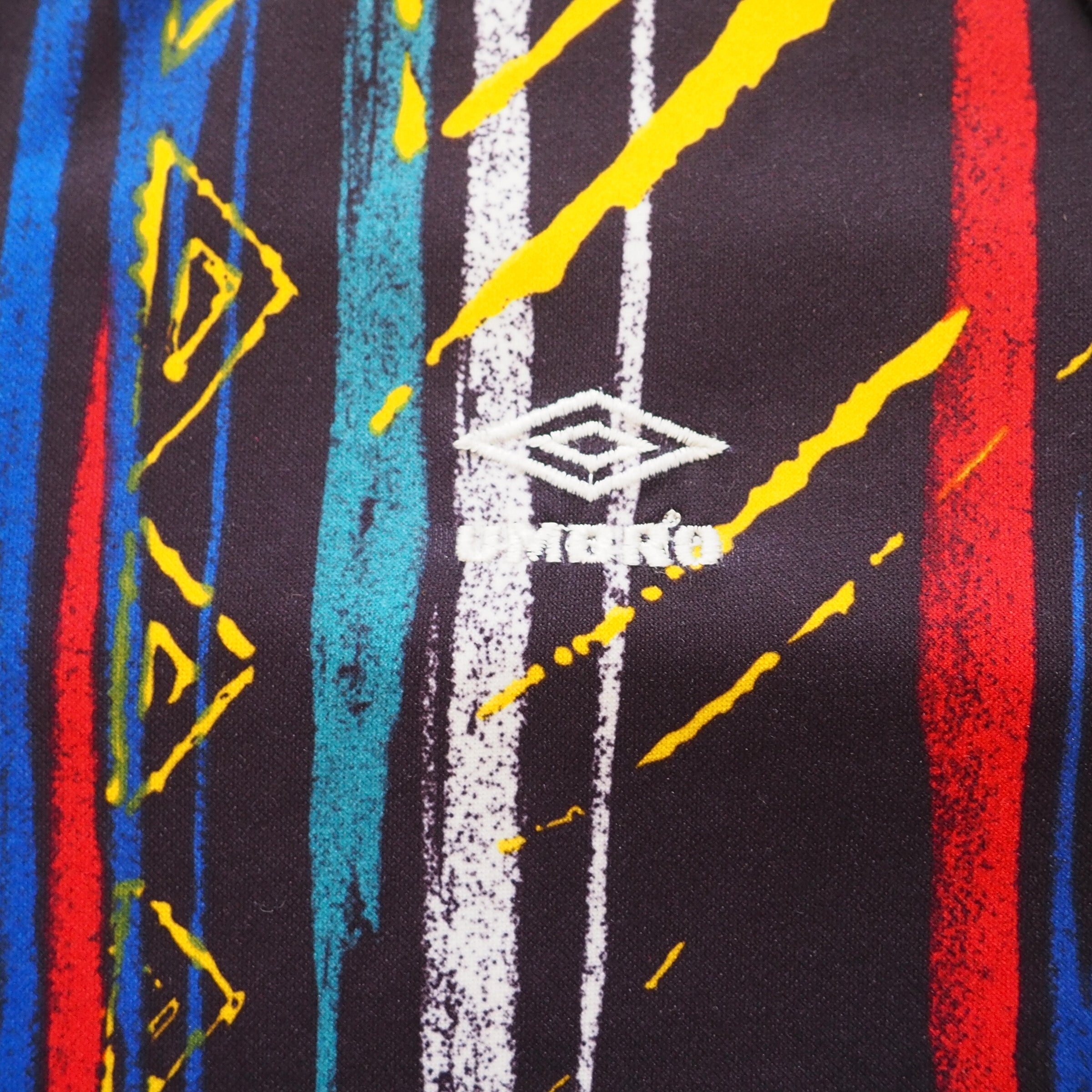 Close-up of a fabric with colorful geometric patterns on a black background and embroidered 'Umbro' logo.