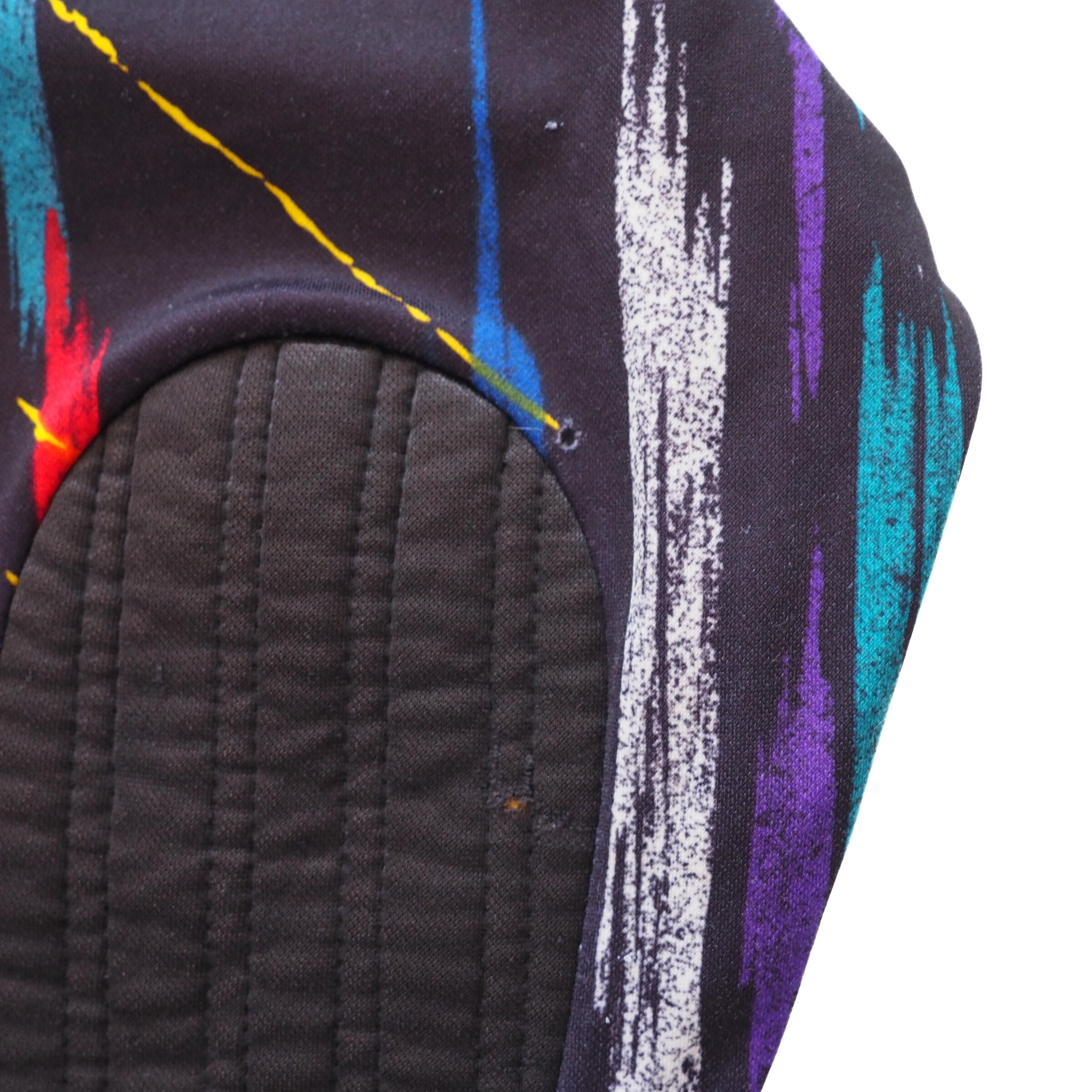 Close-up of padded elbow and small hole in fabric of a vintage Umbro keepers jersey with colorful abstract patterns on a white background