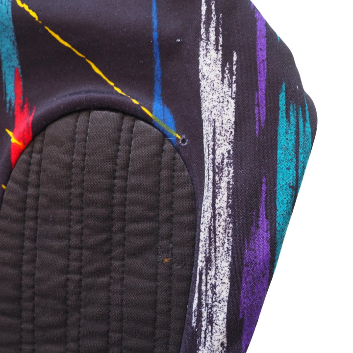 Close-up of padded elbow and small hole in fabric of a vintage Umbro keepers jersey with colorful abstract patterns on a white background