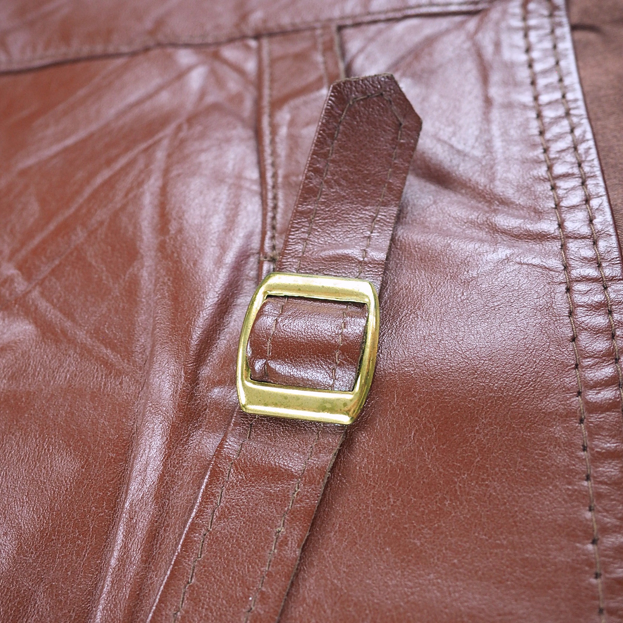 Close up of a brass buckle, leather strap and stitching on a brown leather vest.
