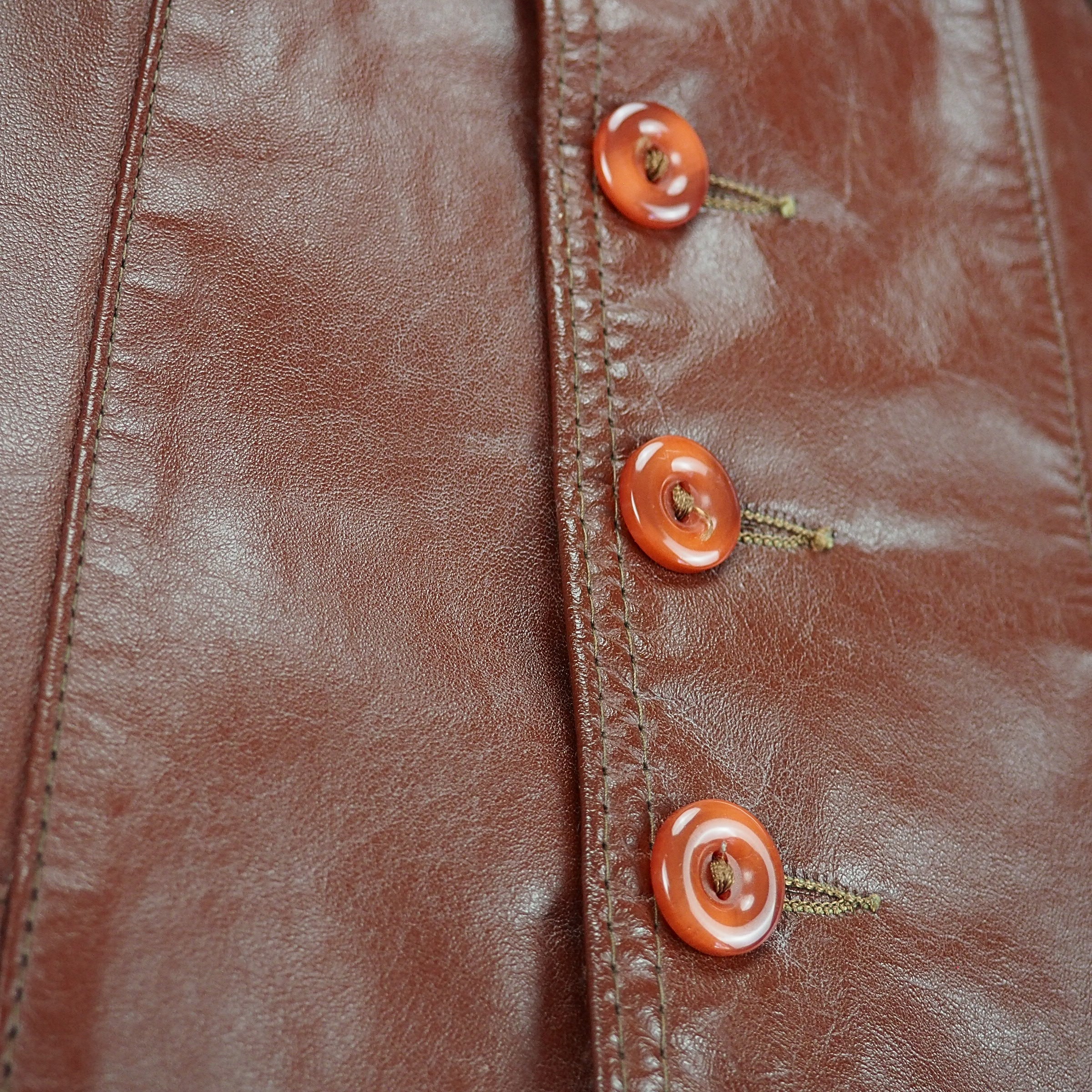 Three amber colored buttons and stitching details on a brown leather vest jacket.
