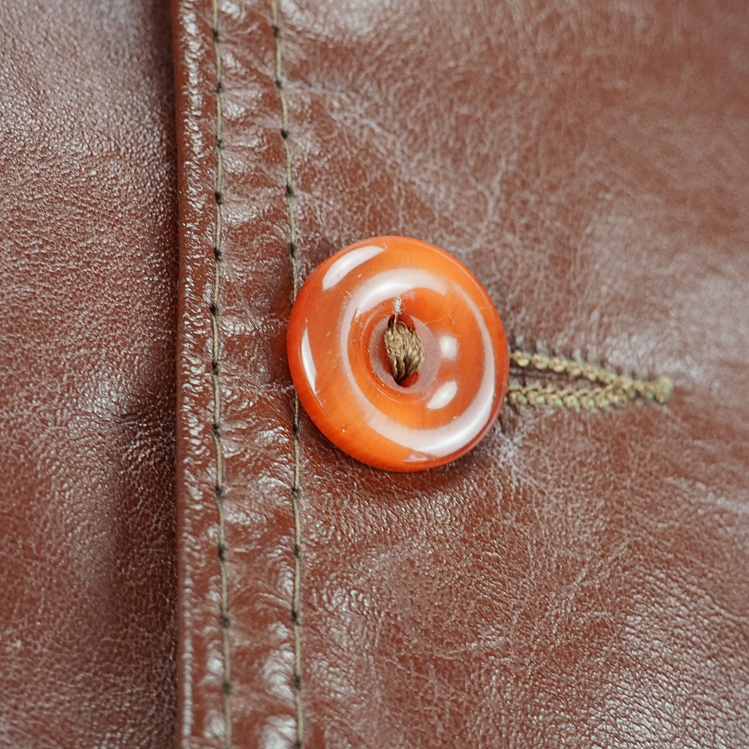 Close up of an amber coloured button and placket stitching on a brown leather vest.