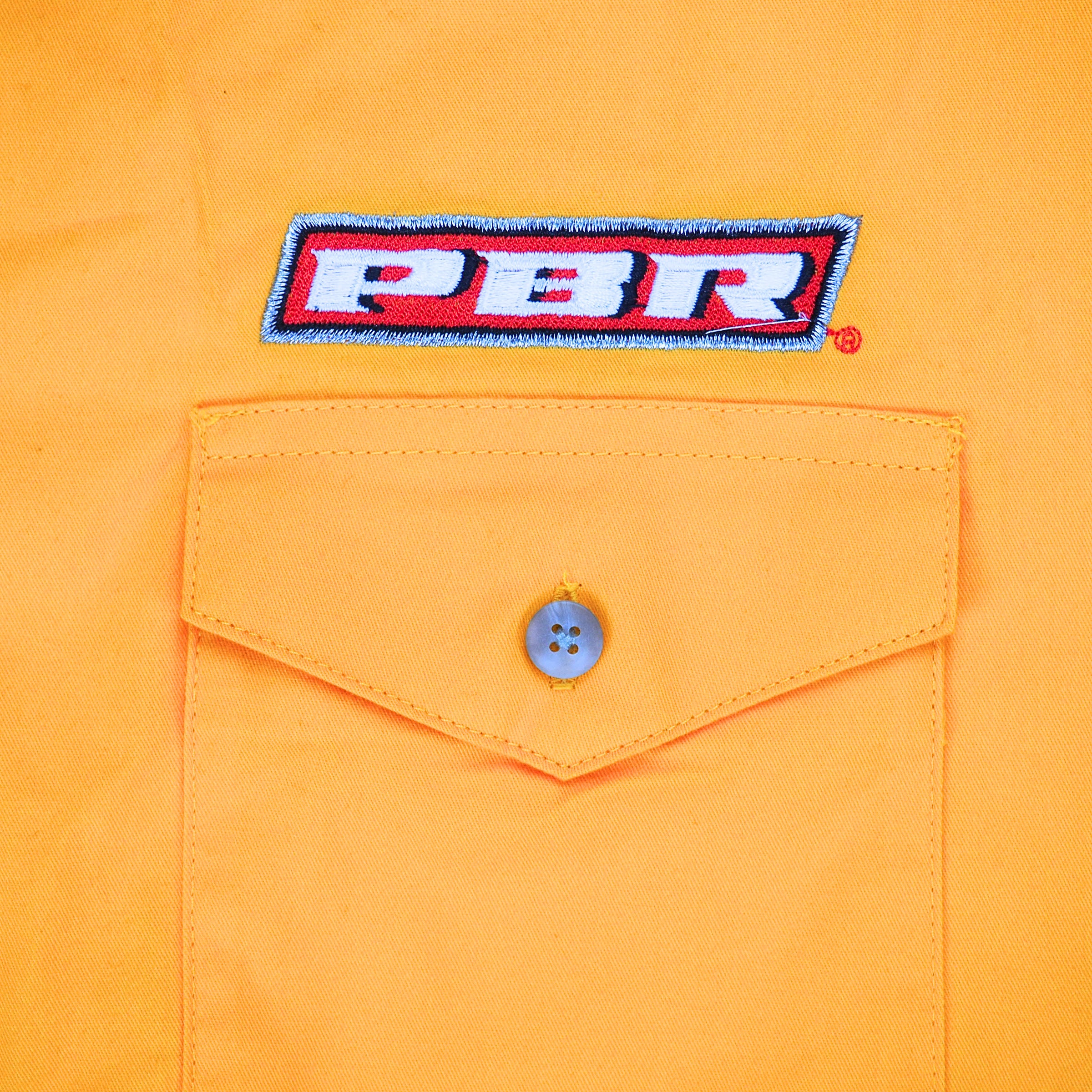 Close up of a dress shirt pocket with flap and button and 'PB' embroidery
