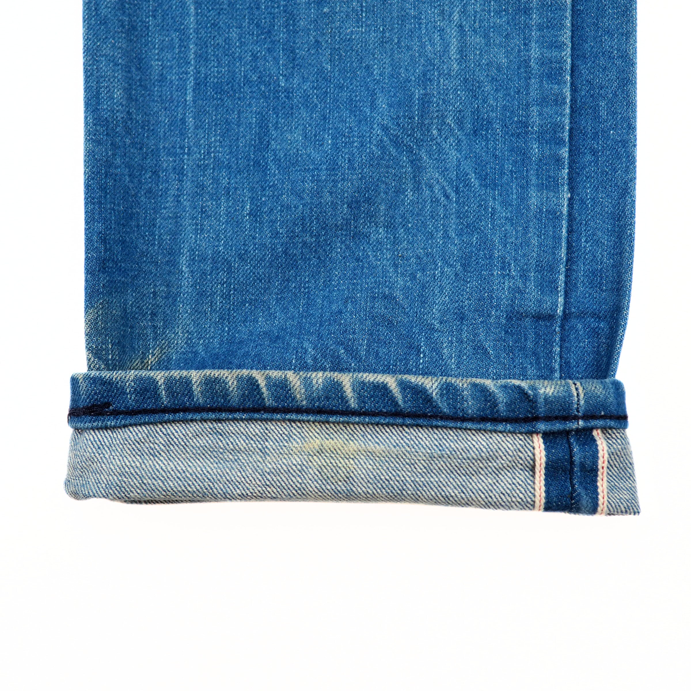Close-up of blue denim jean pant leg cuff with a selvedge seam on a white background