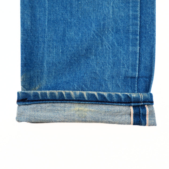 Close-up of blue denim jean pant leg cuff with a selvedge seam on a white background