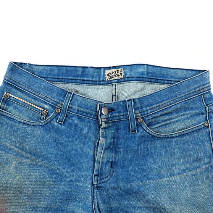 Close-up of the front waist area of a pair of blue jeans with a brand label on a white background
